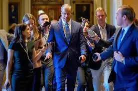 Three suited men walk through a hallway in the U.S. Capitol; one is on the phone and holding documents.